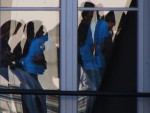 Ombres chinoises de gens attendant sur un quai de train de banlieue, reflétées dans une fenêtre.